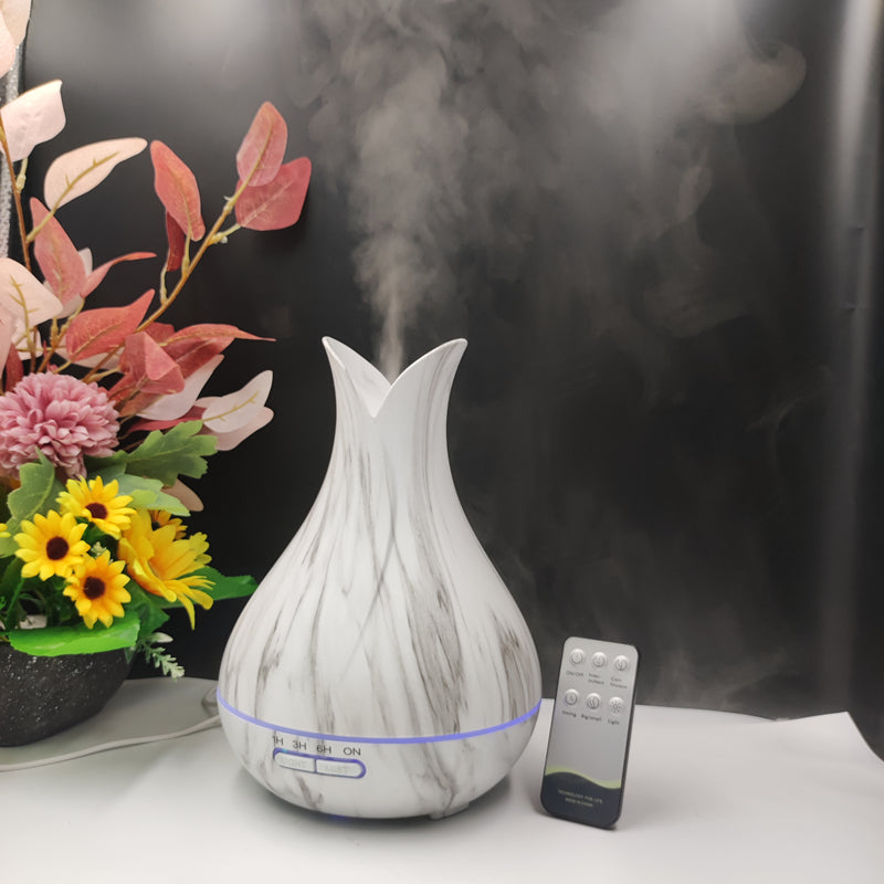 White marble-pattern 500ml diffuser with remote control and LED lights, styled on a white surface with a colorful flower pot on a black background